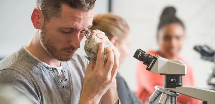 一个学生坐在显微镜前用放大镜观察一块石头