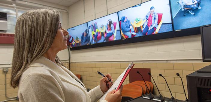 Dr. 克里斯蒂·莱昂斯·格雷厄姆(Christy Lyons Graham)看着学生们在一排电视显示器上练习咨询课程，并做笔记